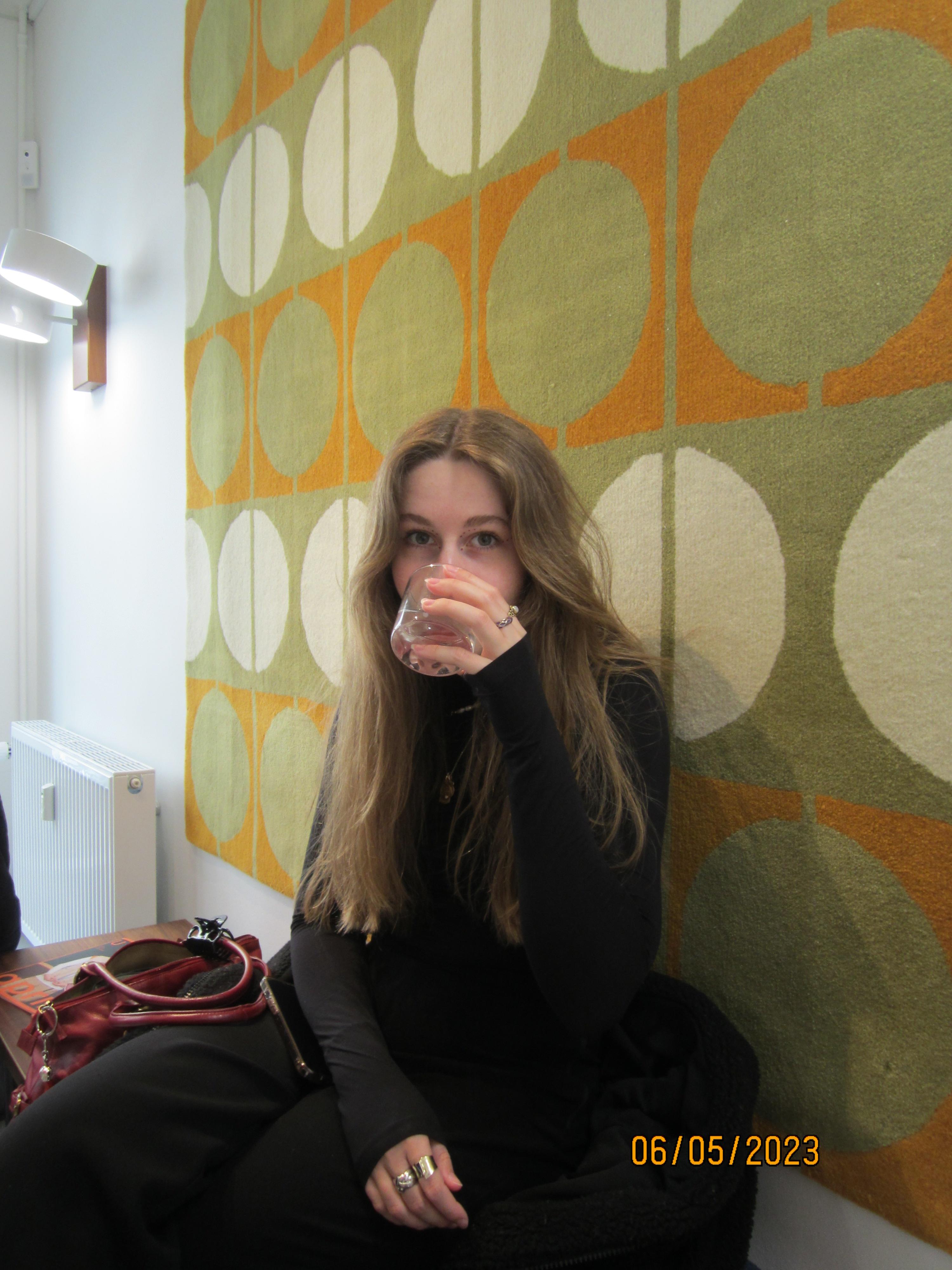Midori Fuchs sipping from a glass in front of a colorful patterned rug